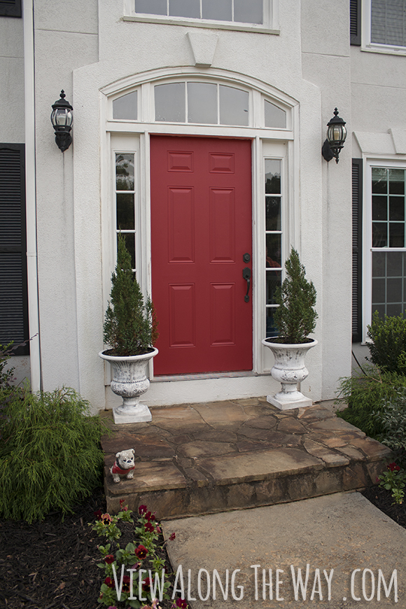 Red front door on a grey house, with spruce trees
