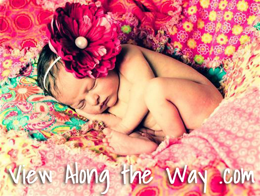 Baby with large flower headband on pink blanket