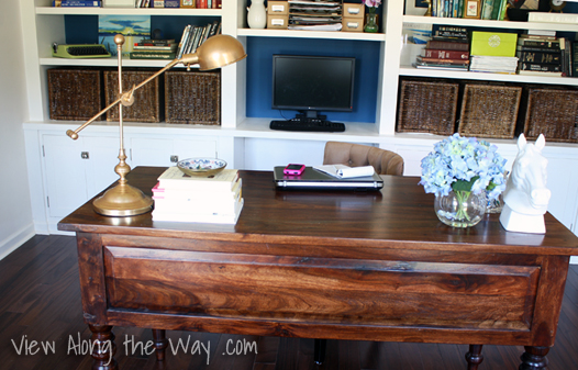 Dark wood desk in home office, with brass task lamp, blue hydrangeas, ceramic horse head statue